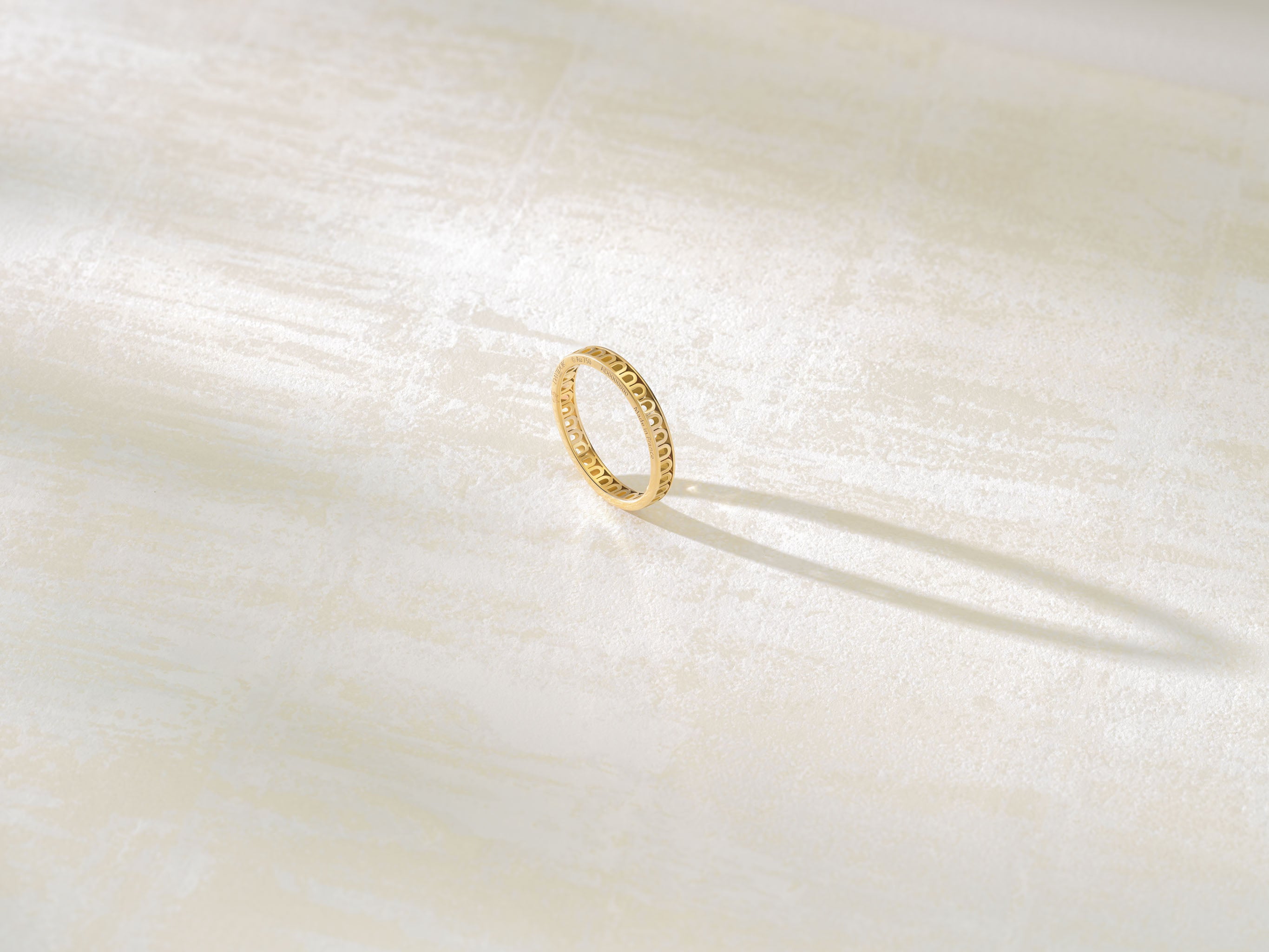 A gold ring with a textured design casts a shadow on a light-colored, textured surface.