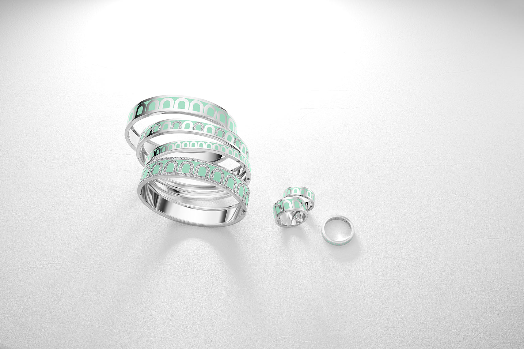 A series of silver spiral rings featuring mint green accents, arranged on a white surface. The shadows of the rings are visible, adding depth to the composition.