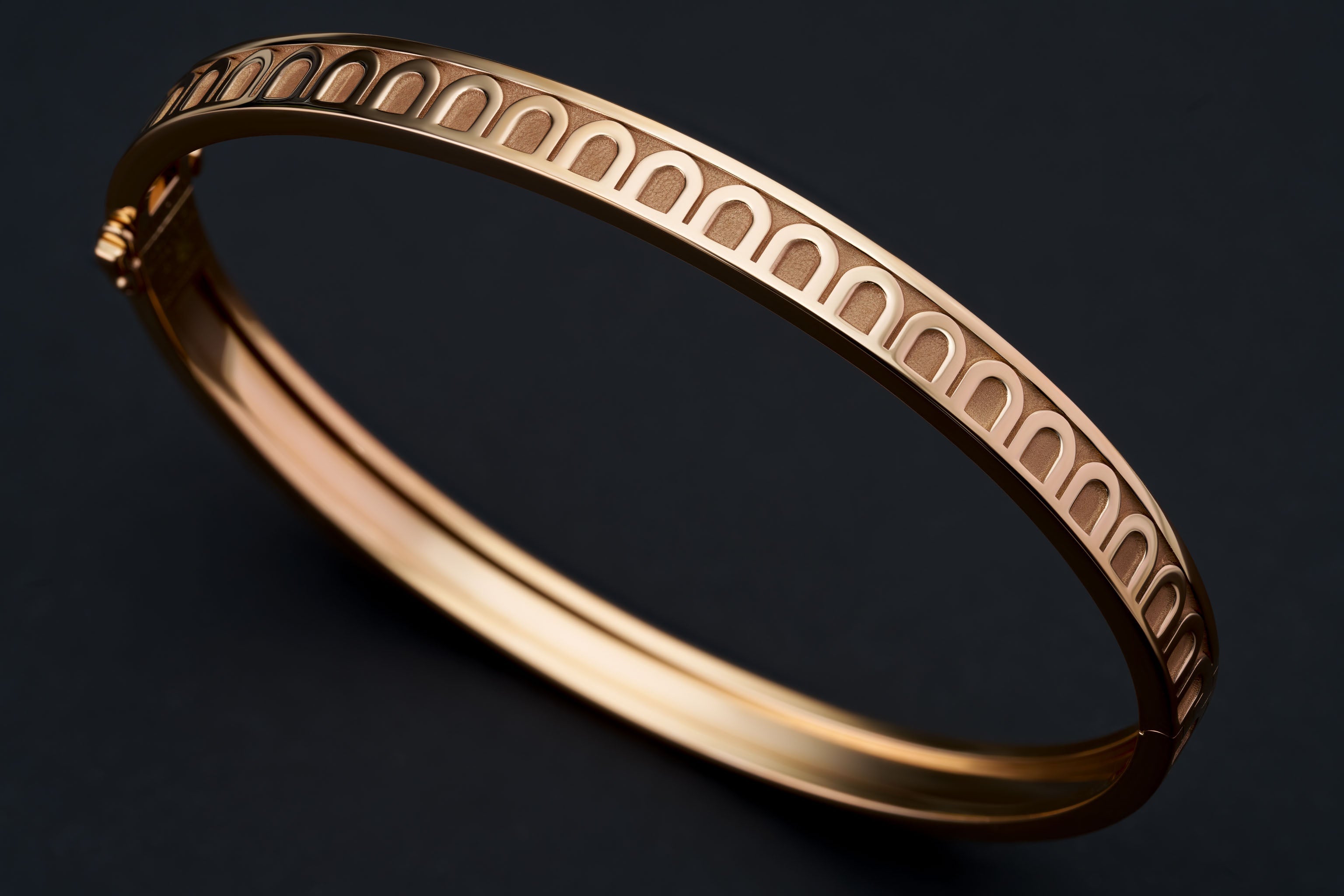 A sleek gold bangle bracelet with an arched cut-out pattern on its surface, displayed on a dark background.