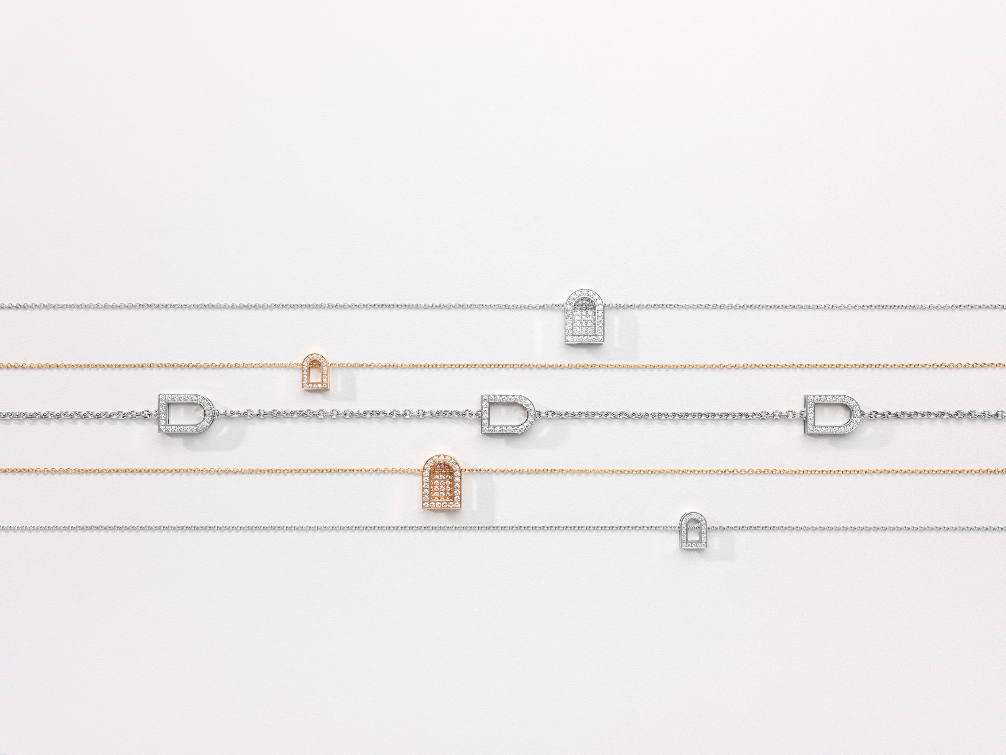 Two elegant bracelets with gold accents and letter D charms on a cylindrical white surface. One bracelet is green and the other is orange, both secured with sleek knots.