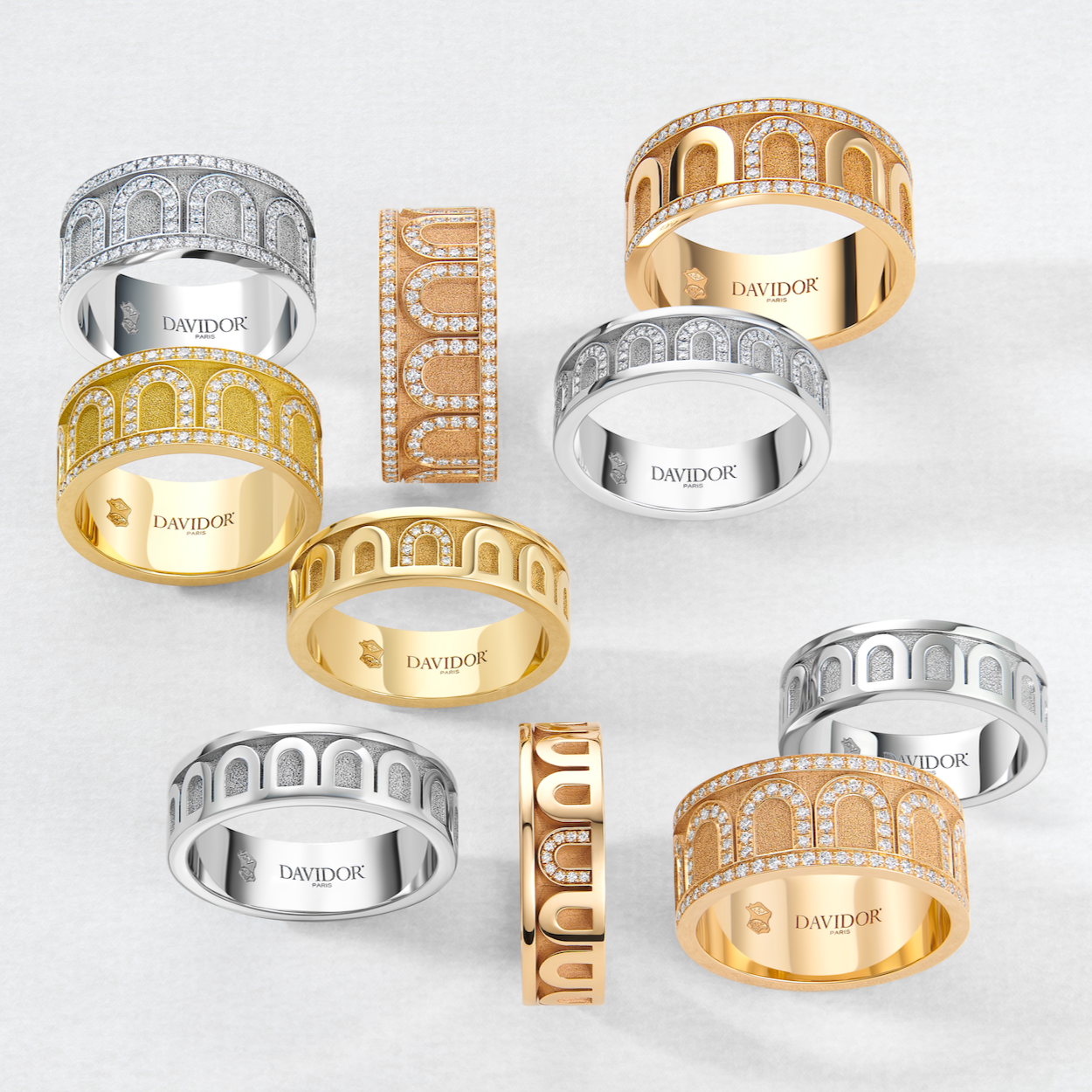 A collection of luxury rings and a bracelet in various metals, including gold and silver tones, adorned with intricate designs and sparkling diamonds, displayed on a light background.