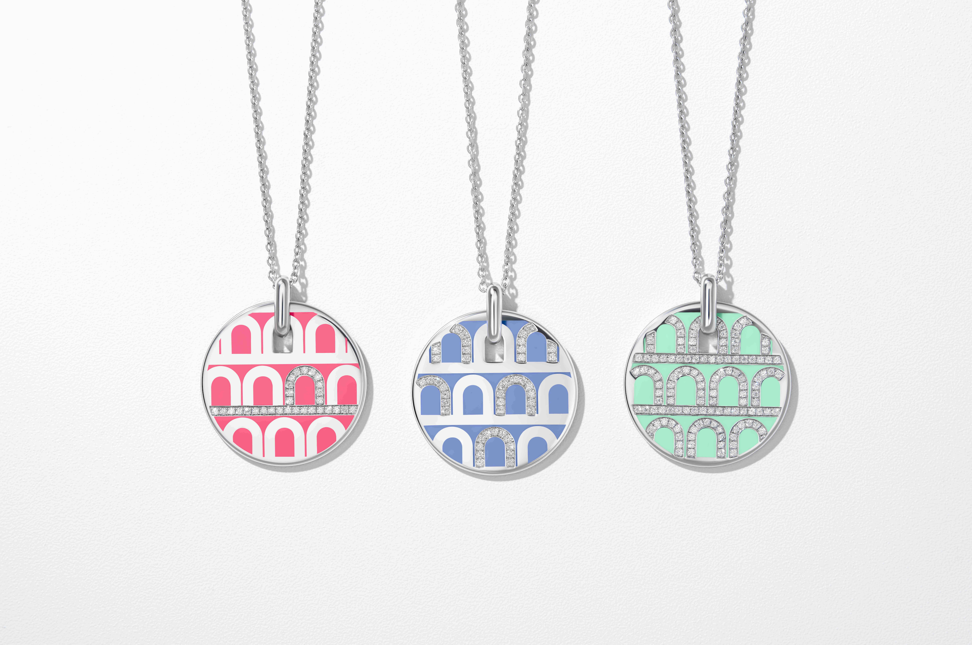 Three silver bracelets with pastel enamel arches in mint green, peach, and blue, displayed diagonally on a textured beige surface.
