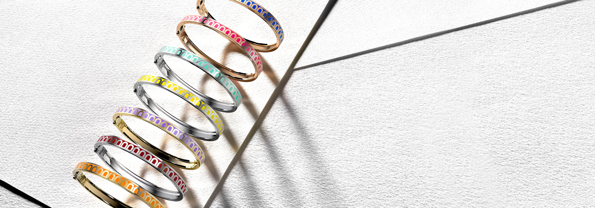 A set of colorful bangles, each with a different color and geometric pattern, displayed diagonally against a textured white background with subtle shadows.