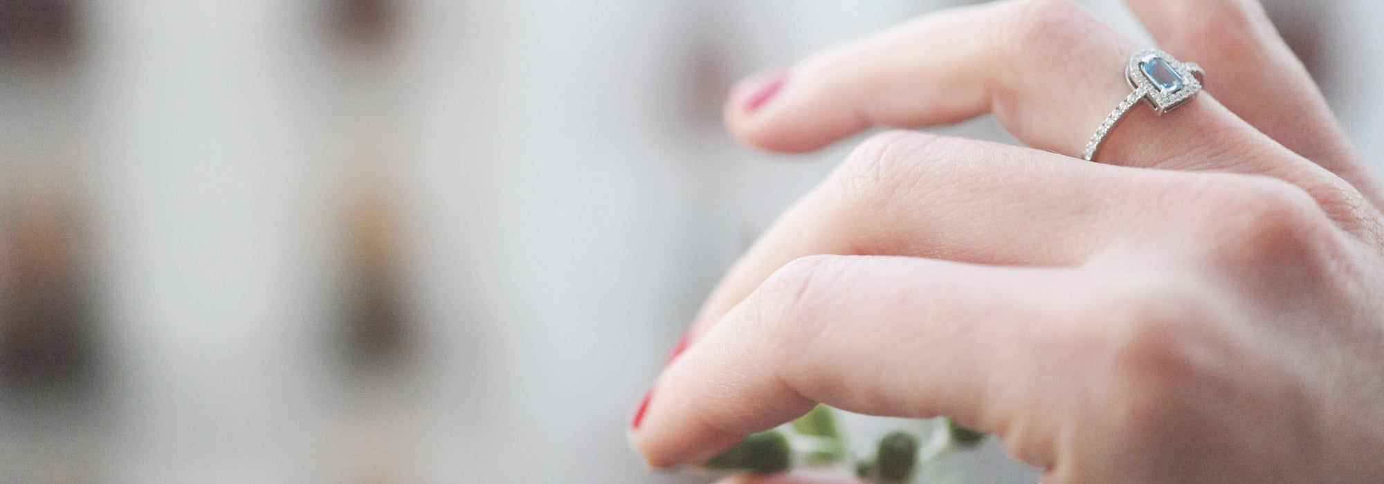 Close-up of a hand with red nail polish, wearing a heart-shaped ring with a small gemstone, gently touching a plant.