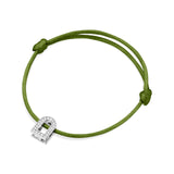 A silk cord bracelet in green, showcasing an adjustable knot design and featuring the L'Arc Voyage Charm PM from the Paris Atelier collection. The 18k white gold charm is embellished with Galerie diamonds and small clear stones resembling a silver padlock.