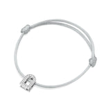 The L'Arc Voyage Charm PM bracelet, featuring an 18k white gold horseshoe-shaped charm embellished with Galerie diamonds, is elegantly displayed on a plain white background. This sophisticated piece from the Paris Atelier collection is set on a thin silk cord with an adjustable knot design.