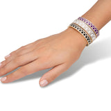 A hand wears four L'Arc de DAVIDOR Bangle MM bracelets in 18k yellow gold with lacquered ceramic (purple, white, pink, black) and Palais Diamonds—each showcases a repeating arch pattern—set against a white background.